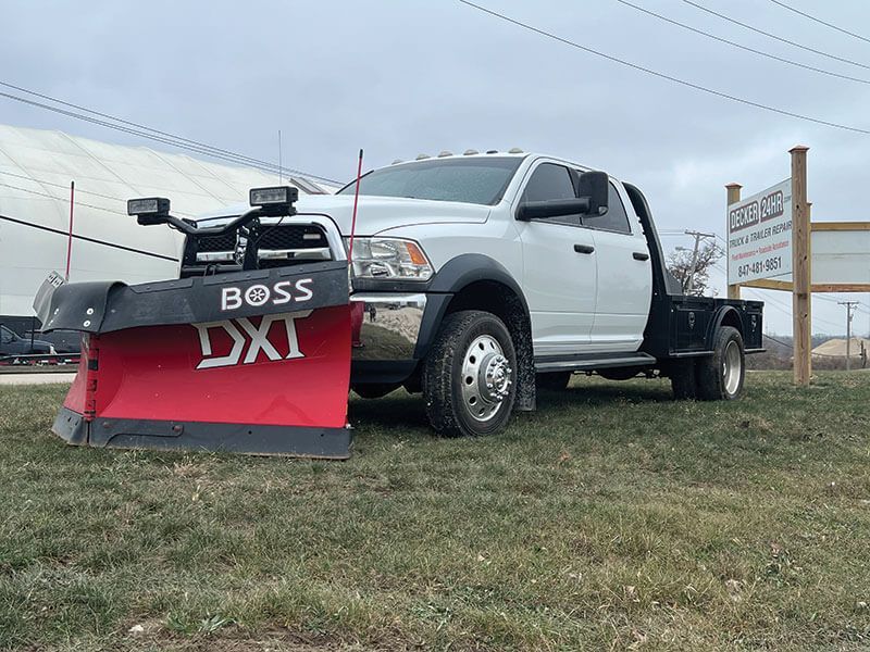 White snow plow truck with a Boss DX1 plow on a grassy area.