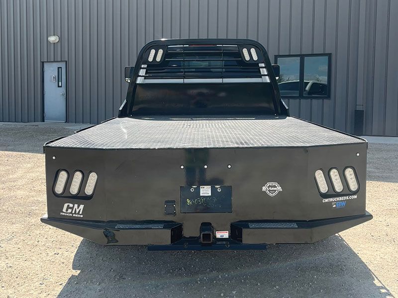 Black flatbed truck with headache rack, parked outside a building.