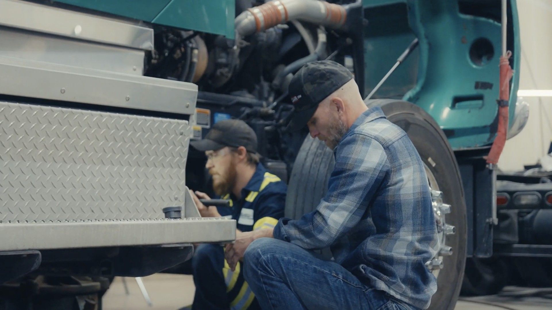 Trucker in red overalls inspects a red semi-truck near the cab.