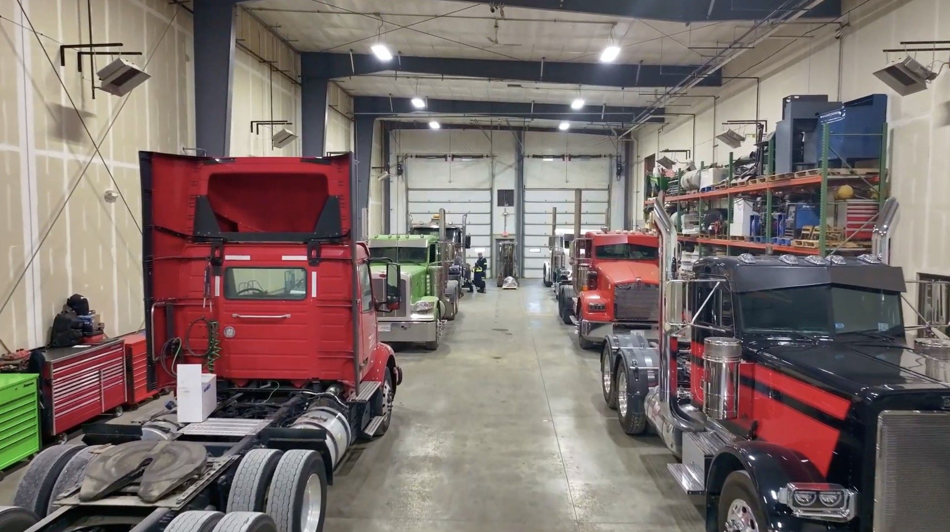 Trucks in a repair shop; vehicles are white, red and blue, with tools, on a red floor.