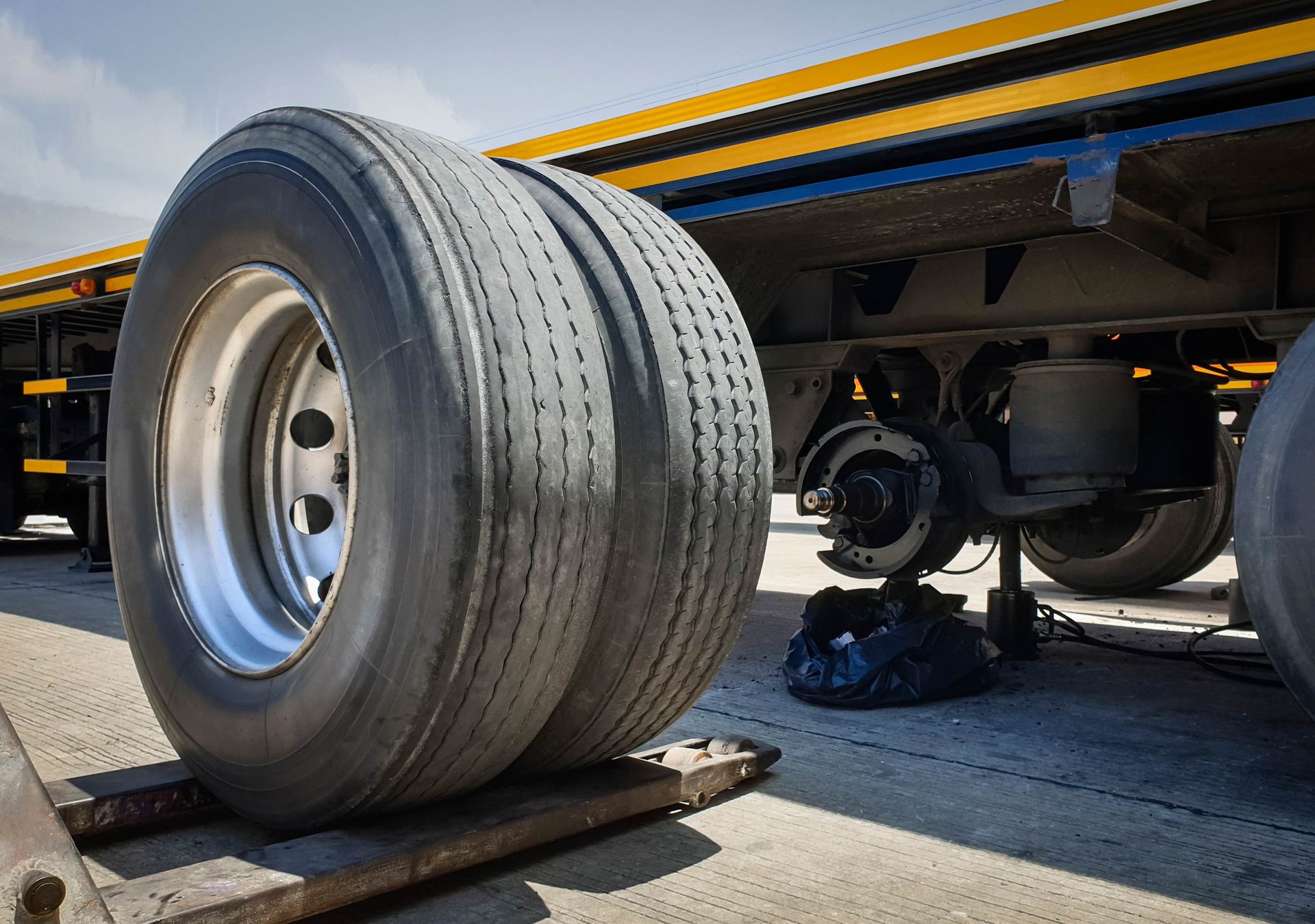 Two large truck tires on a trailer, one slightly in front of the other, on a paved surface.