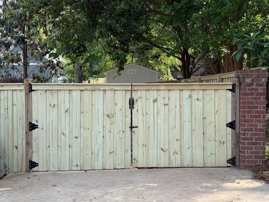 Wooden double gate with black hardware, flanked by brick and wood posts, gravel driveway.