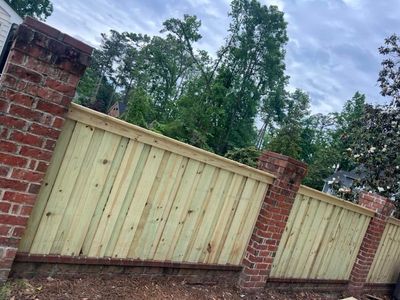 Brick pillars support a wooden fence. Fresh, light-colored wood contrasts with aged red brick.