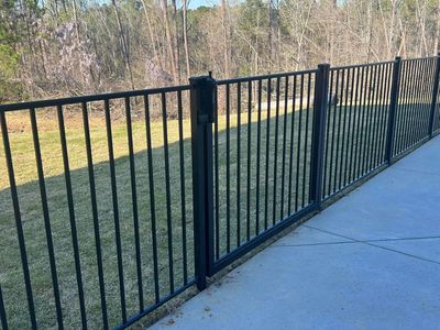 Black metal fence on concrete patio, enclosing green grass and trees.