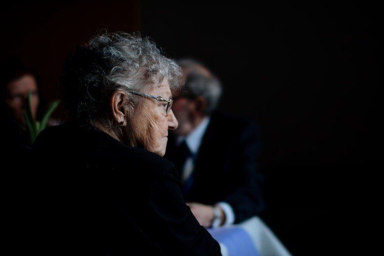 A white old lady wearing dark blue dress and looking on her right side.