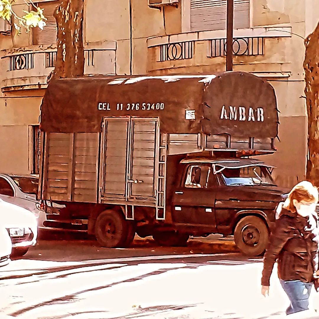 Camioneta negra con caja cubierta estacionada en una calle de la ciudad; una persona pasa caminando.