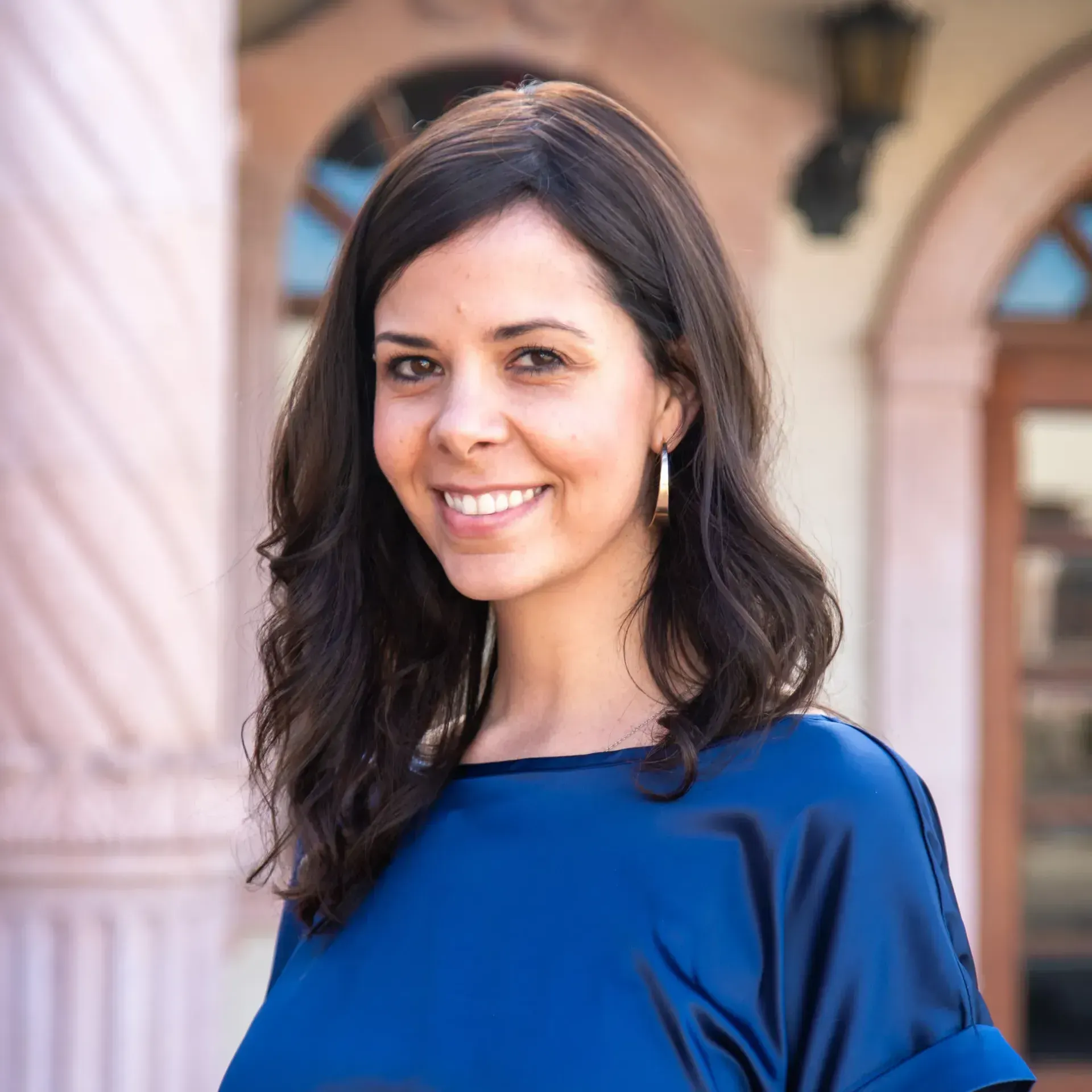 A woman wearing a blue shirt and earrings is smiling for the camera.