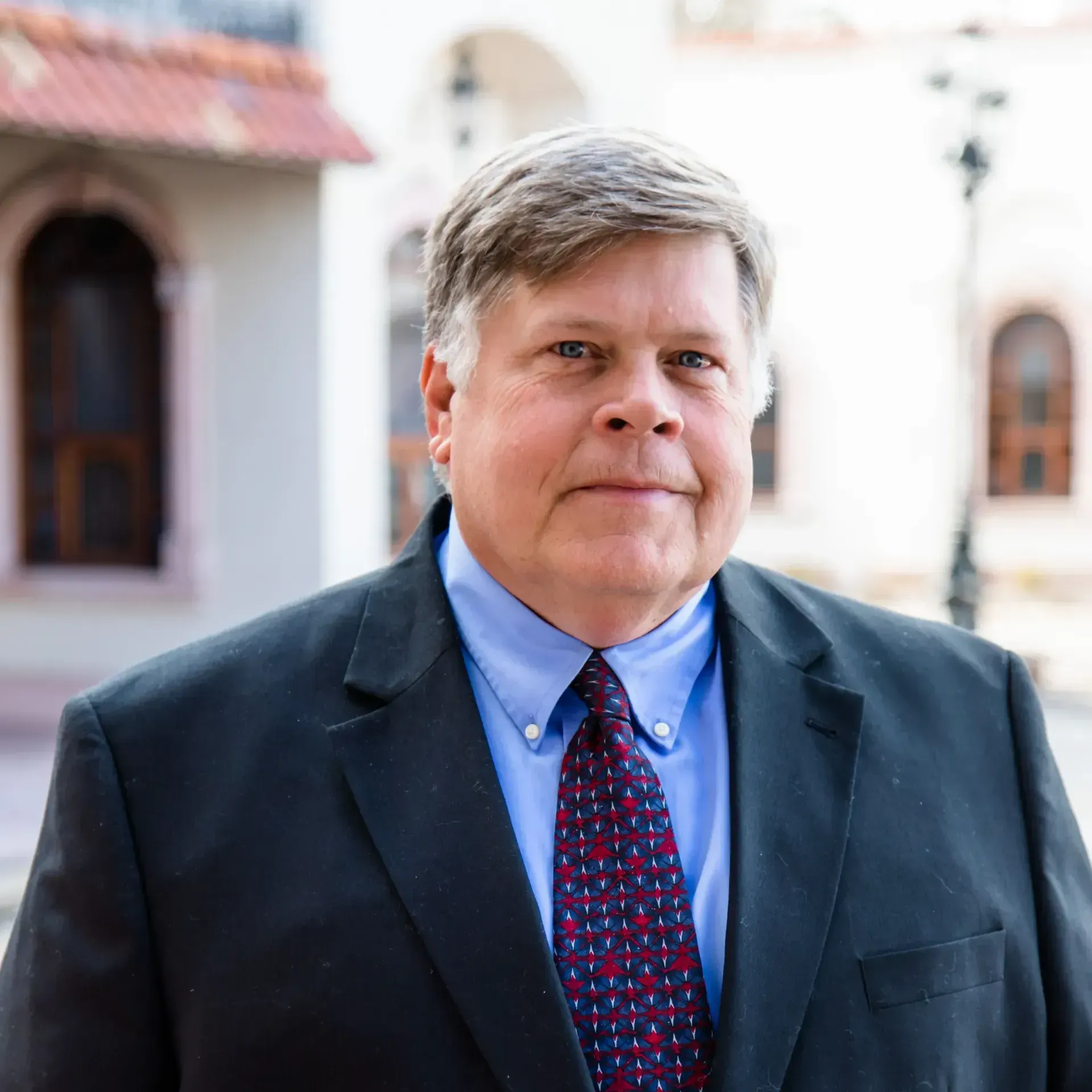 A man in a suit and tie is standing in front of a building.