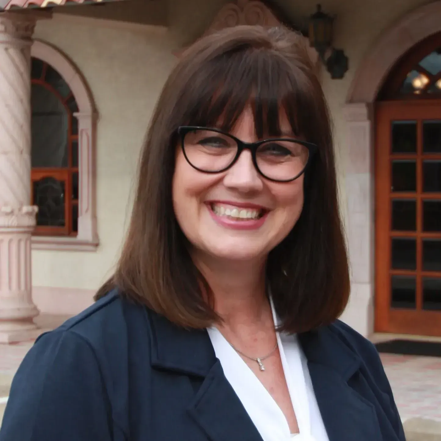 A woman wearing glasses and a blue jacket smiles for the camera