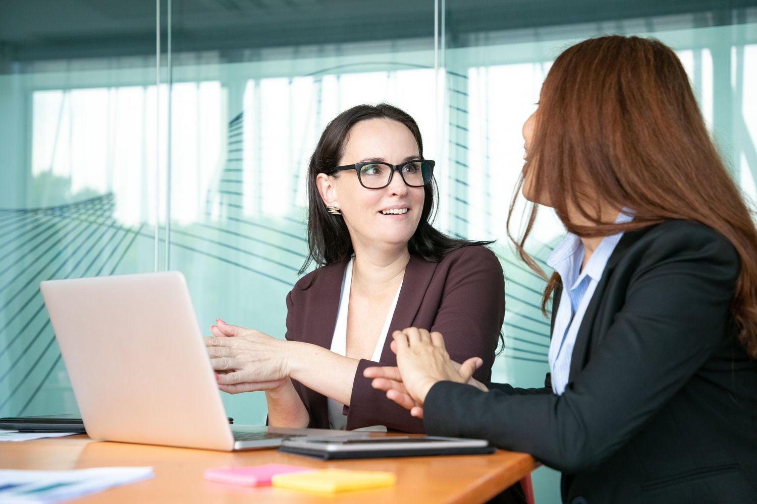 Two coworkers talking at a table with a laptop in a bright office