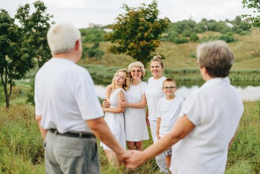 Group holding hands in a grassy field, smiling at each other outdoors.