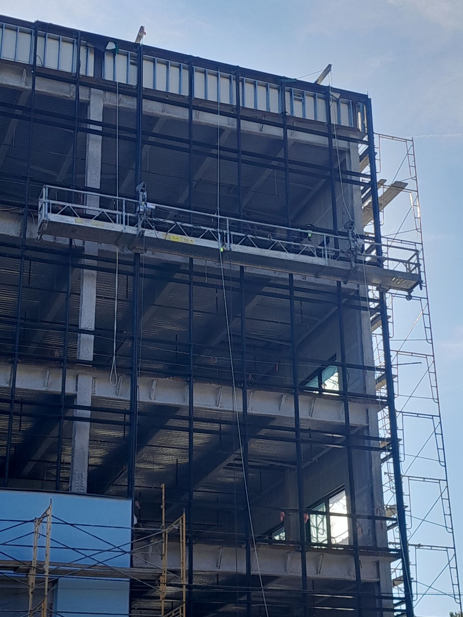 A large building under construction with scaffolding and a blue sky in the background