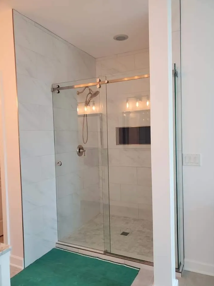 A bathroom with a sliding glass shower door and a green rug.