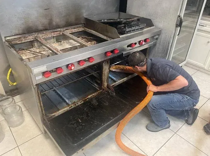 A man is cleaning a stove with a hose in a kitchen.