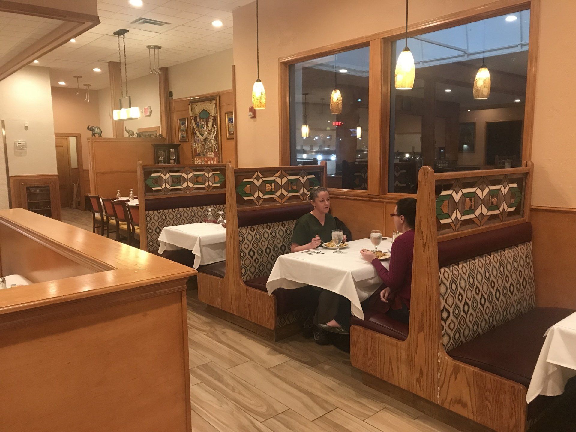 Restaurant interior with booths, tables, and two women seated at one, by a window.
