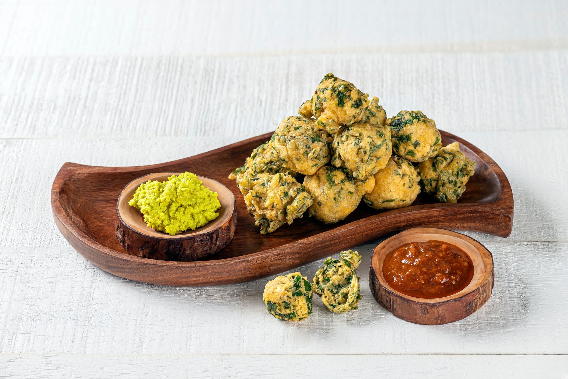 Fried spinach balls with two dipping sauces on a wooden platter.