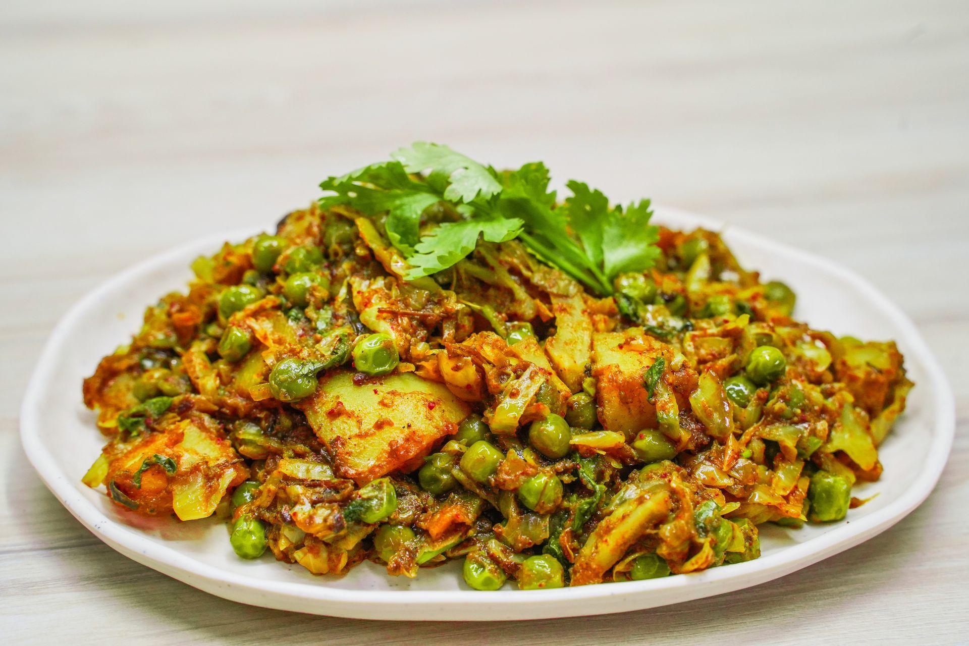 A plate of Indian-style potato and pea vegetable curry, garnished with cilantro.