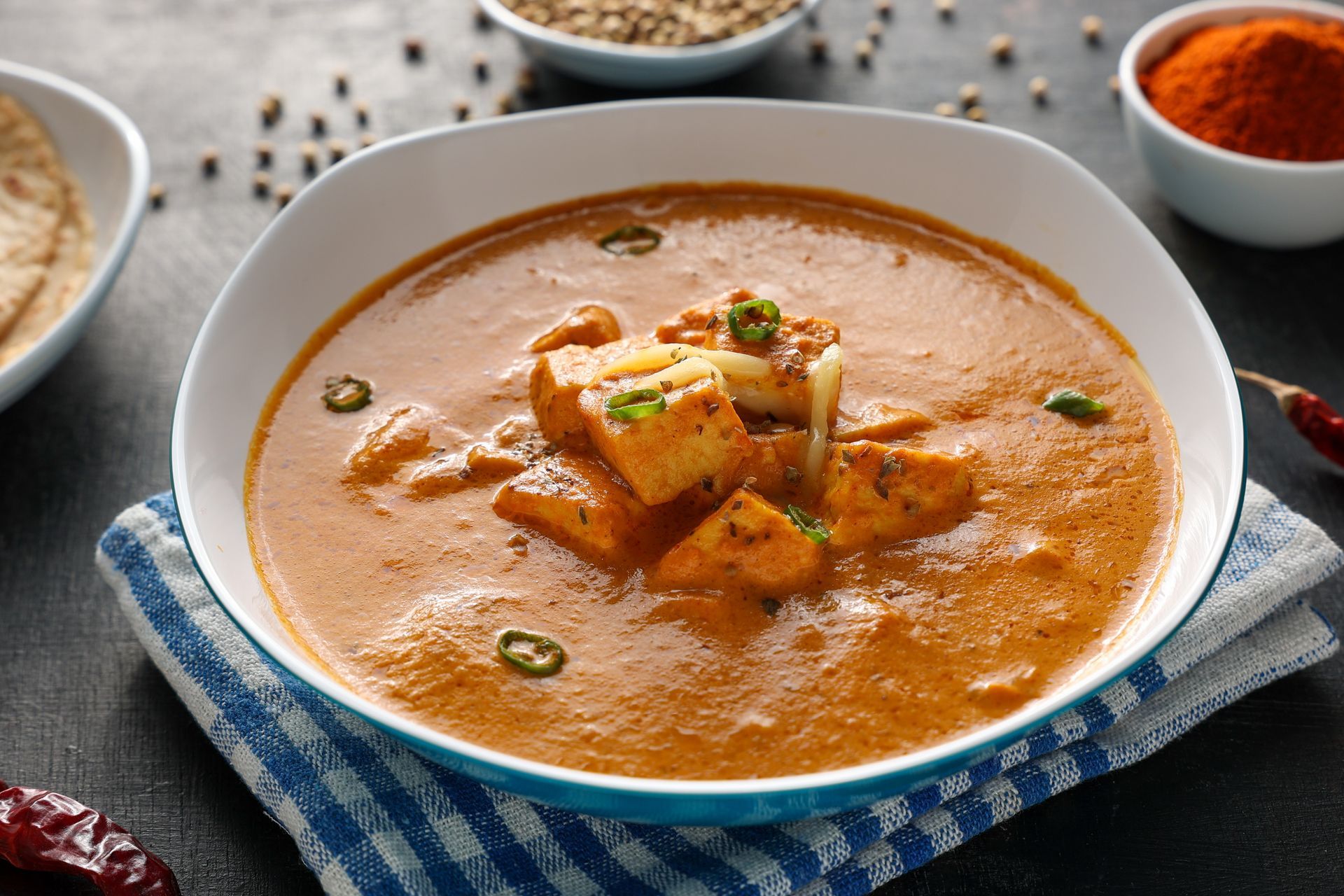 Bowl of creamy orange paneer (Indian cheese) curry, garnished with chilies.