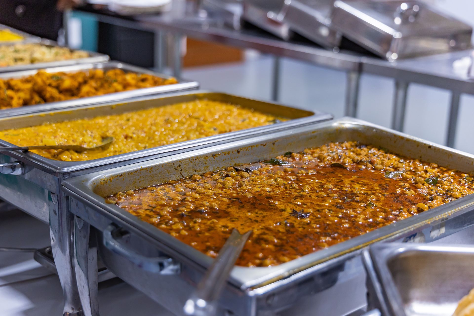 Buffet with various Indian dishes in silver warming trays.
