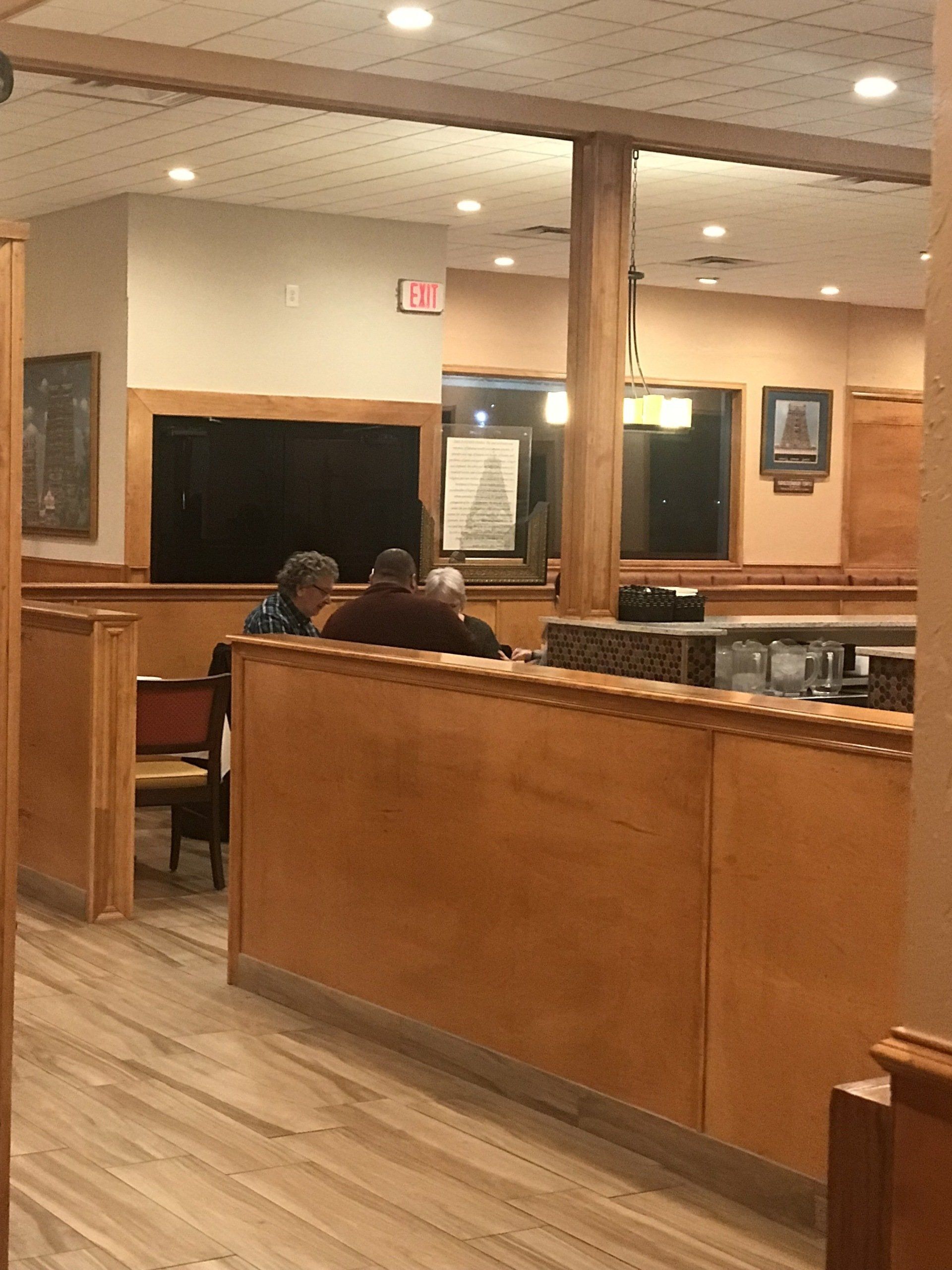 People are sitting at tables in a restaurant with an exit sign in the background