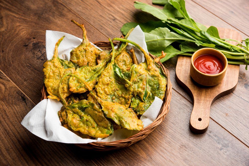 A basket of fried spinach leaves next to a bowl of ketchup on a wooden table.