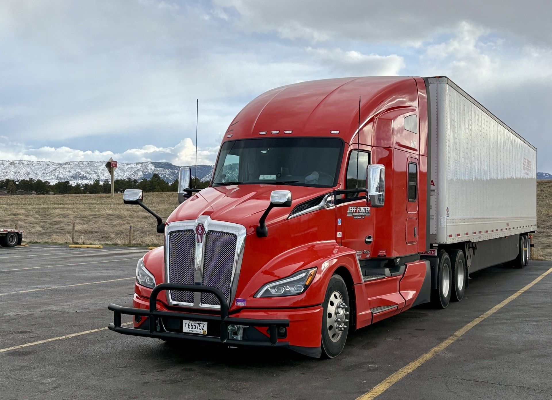 Red semi-truck with white trailer parked in a lot under cloudy skies