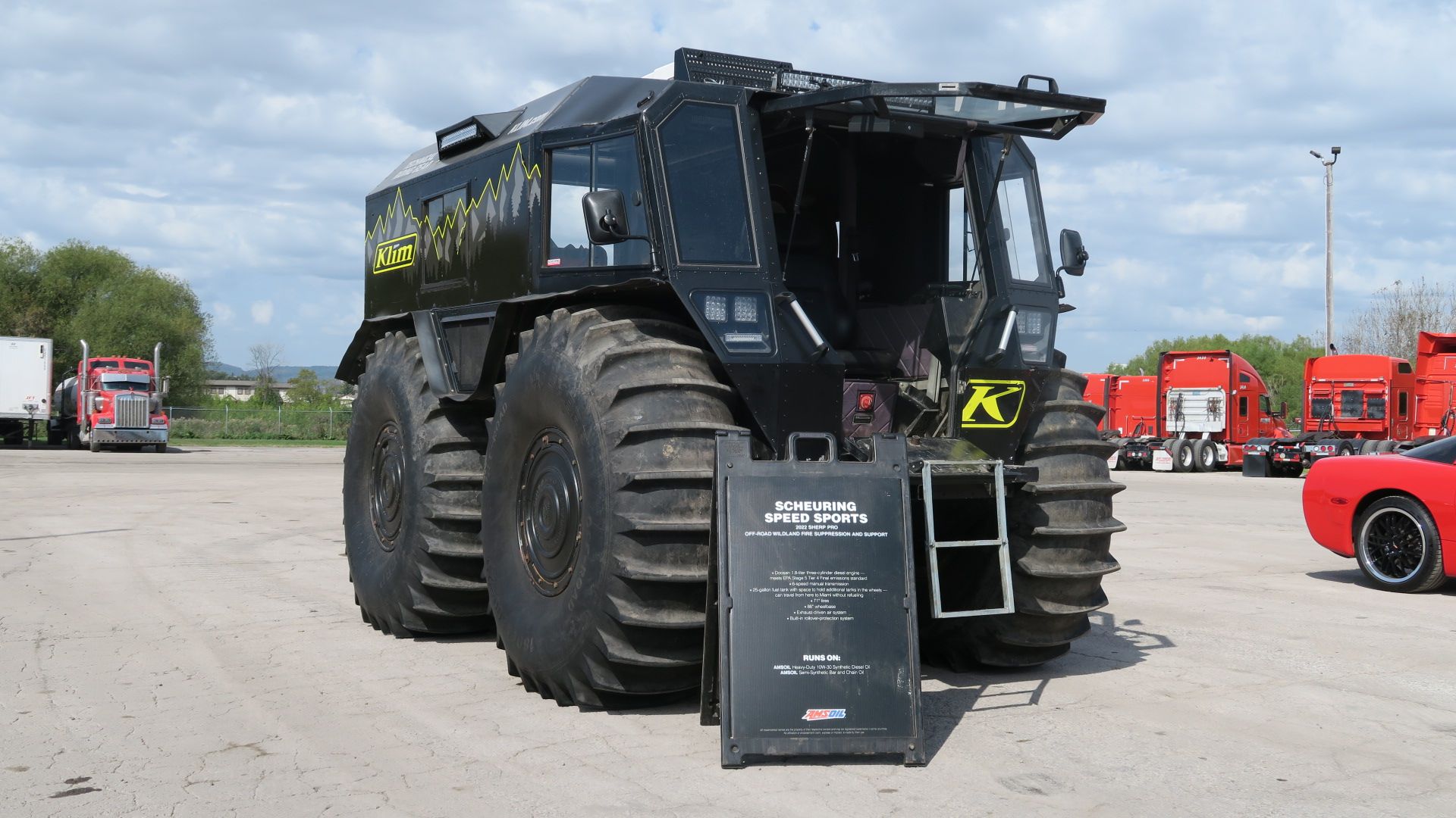 A large black vehicle is parked in a parking lot next to a red car.