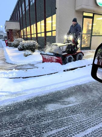 A snow plow is parked in the snow in front of a building.