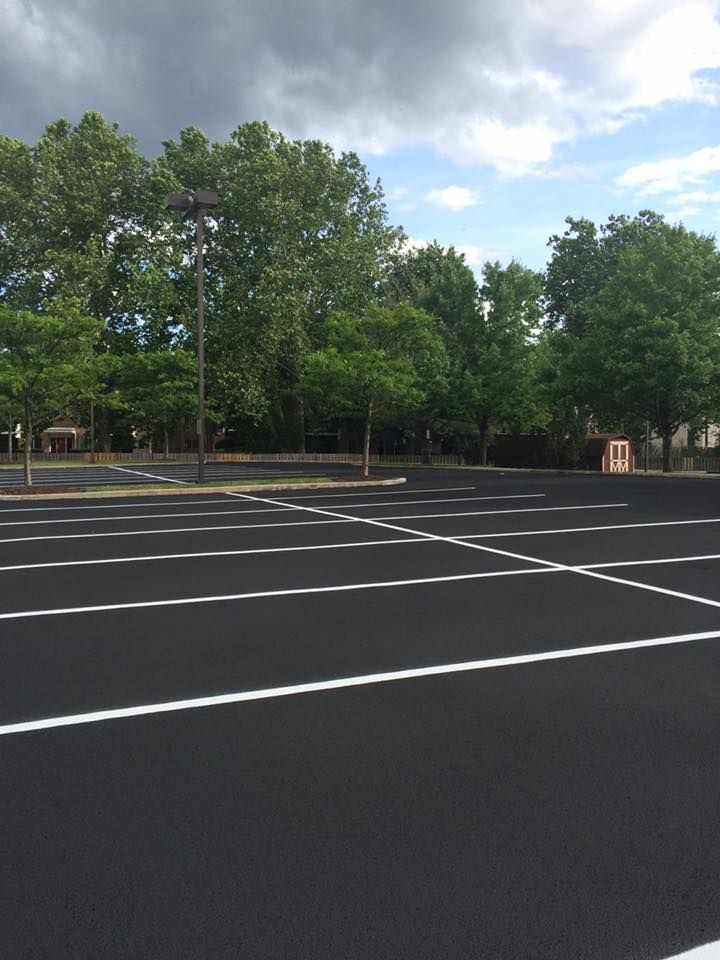Empty asphalt parking lot with white lines, trees, and cloudy sky.