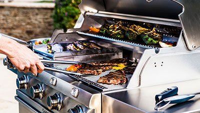 a person is grilling meat and vegetables on a stainless steel grill  | Ashland, MA | Lunkers Outfitters