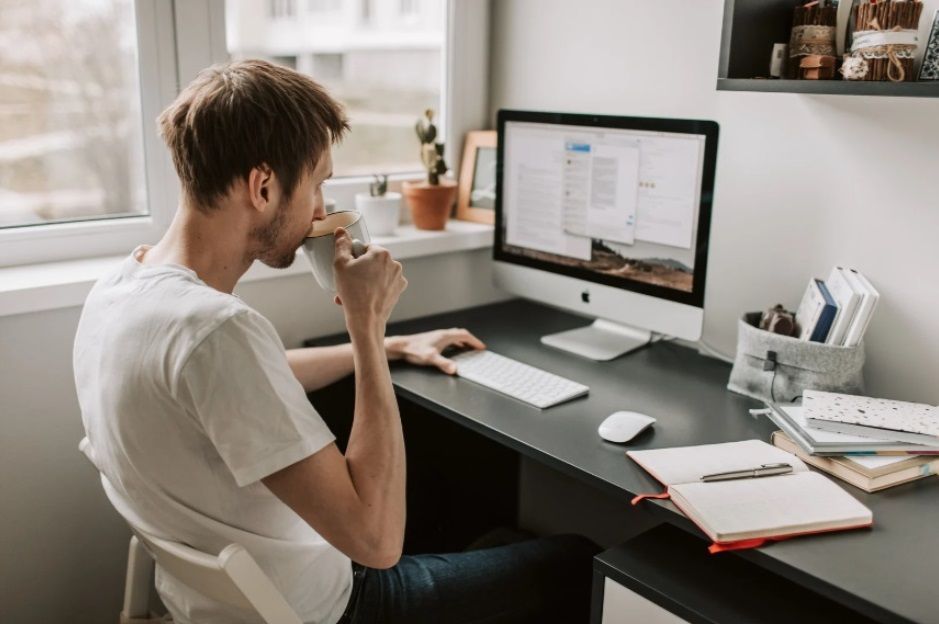 Homme devant son bureau en télétravail avec un tasse de café. 