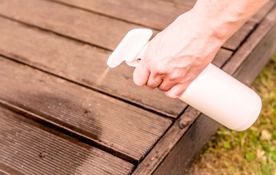 une personne qui pulvérise un remède de grand-mère sur sa terrasse en bois pour la protéger des insectes xylophages