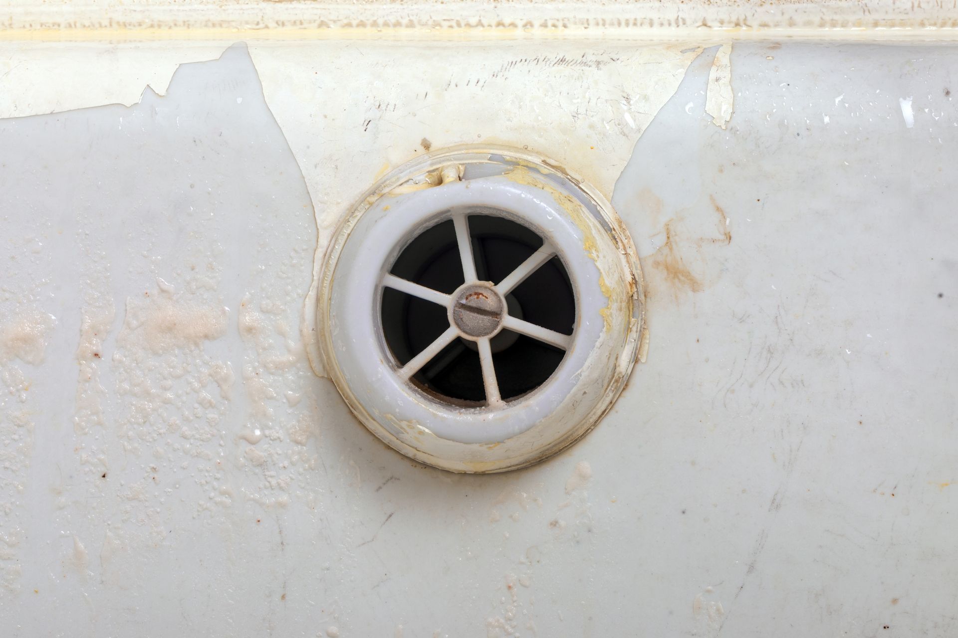 Round white vent with black grille on a stained off-white wall or panel.