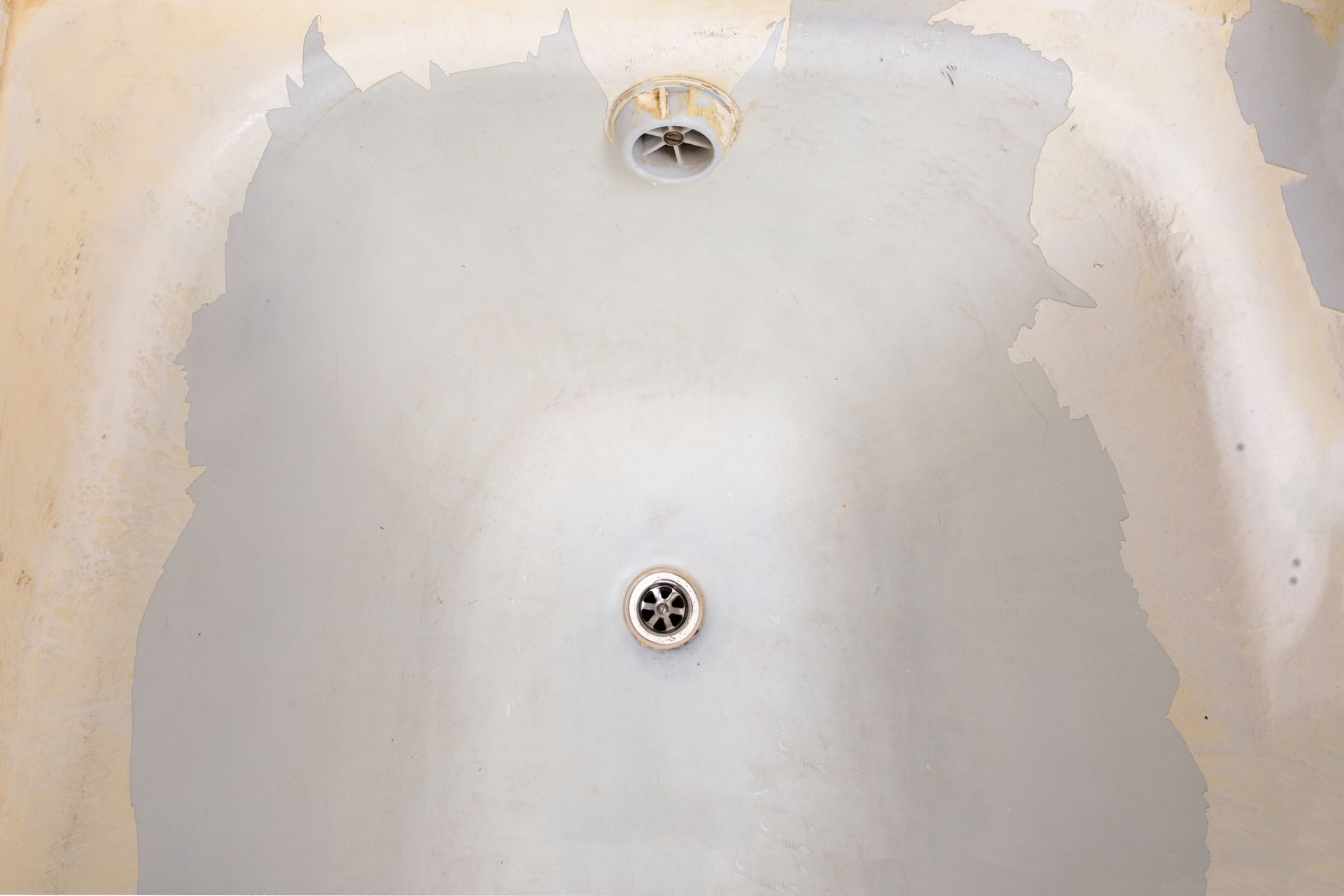 Empty bathtub with stained, patchy white surface and visible drain and overflow opening