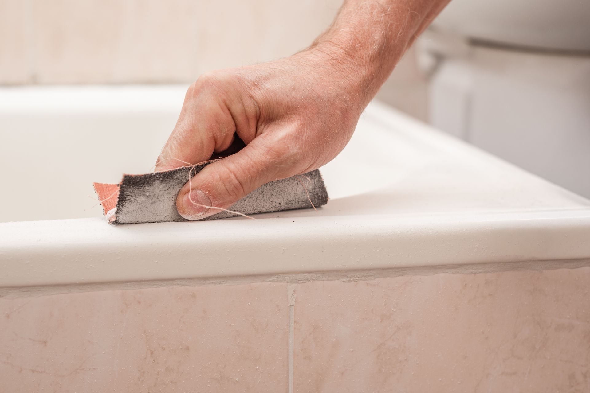 Hand sanding a bathtub edge to prepare surface for refinishing.