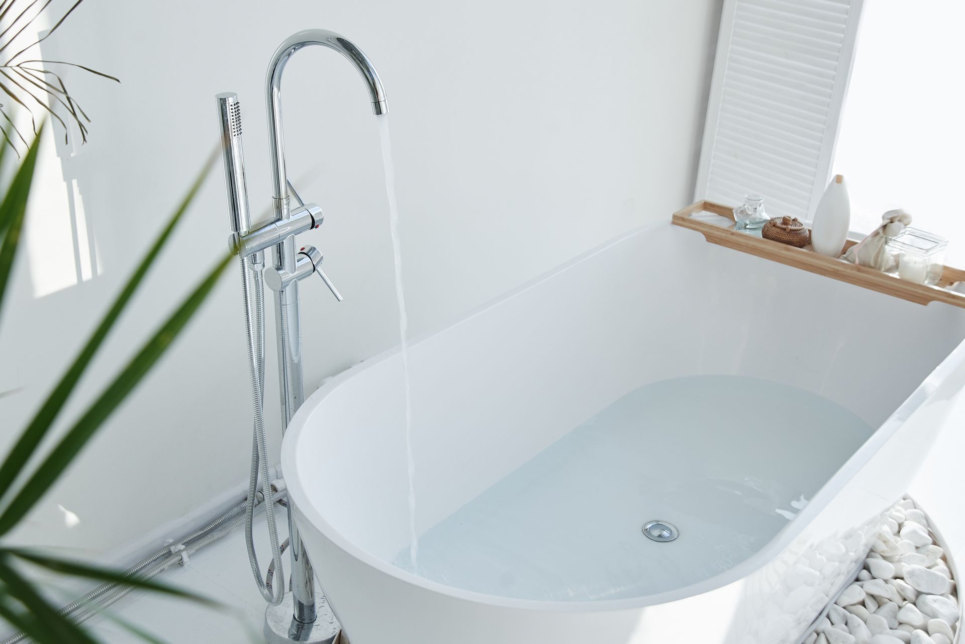 A modern freestanding bathtub filling with water from a sleek chrome faucet in a minimalist bathroom.