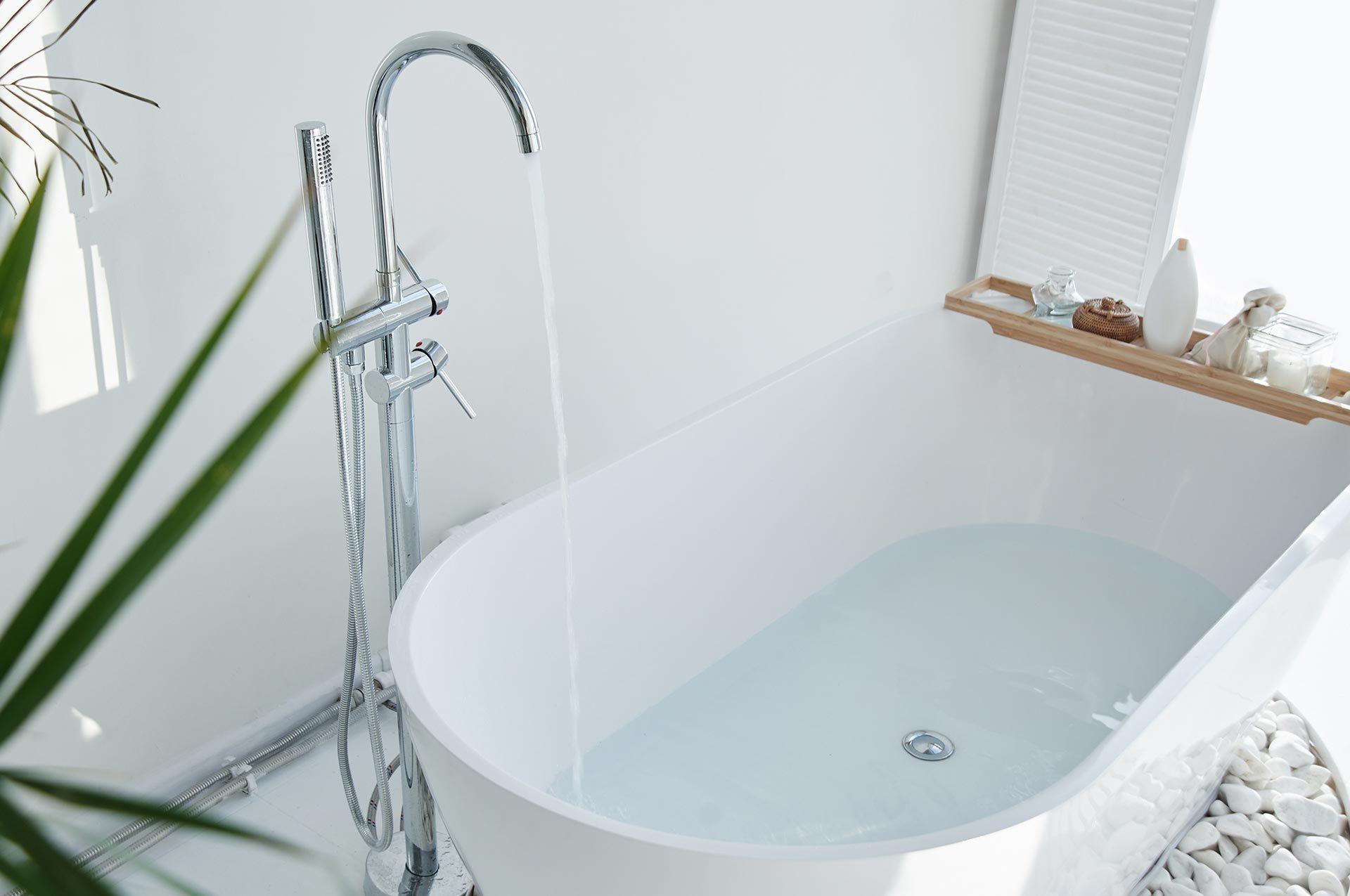 A modern white bathtub with a chrome faucet fills water in a bright minimalist bathroom.