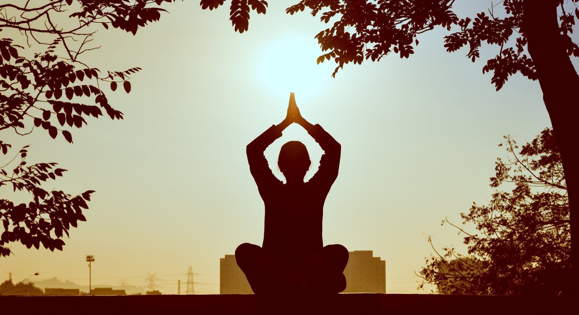Meditierende Silhouette im Schneidersitz mit erhobenen Händen zur Sonne – Ausdruck von innerer Ausrichtung, Achtsamkeit und Dankbarkeit.