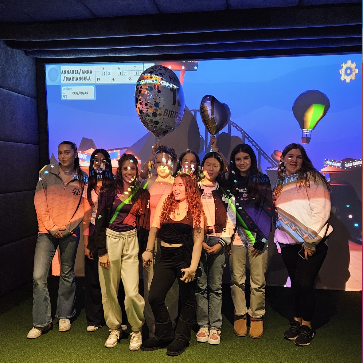 Group of young women smiling in front of a screen with hot air balloons. They are in a room with a simulated background.