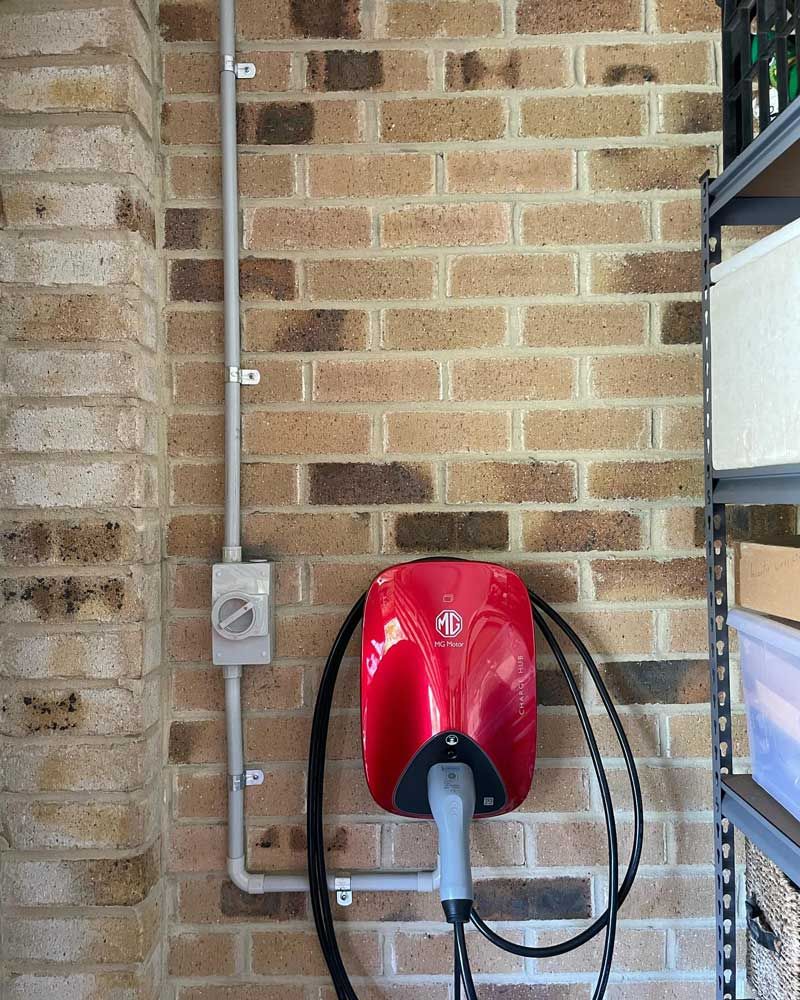 A Red Electric Car Charger Installed on a Brick Wall — Ocean Air Electrical in Tweed Heads, NSW