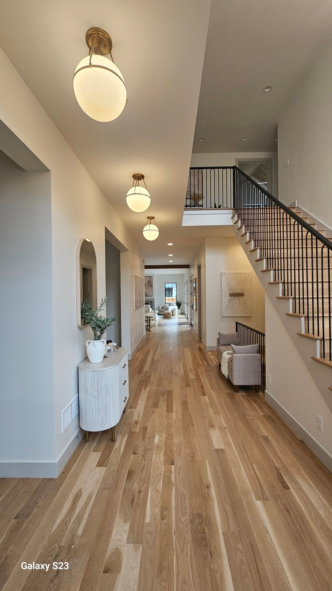 Long hallway with hardwood floors, white walls, and stairs leading to an upper level.