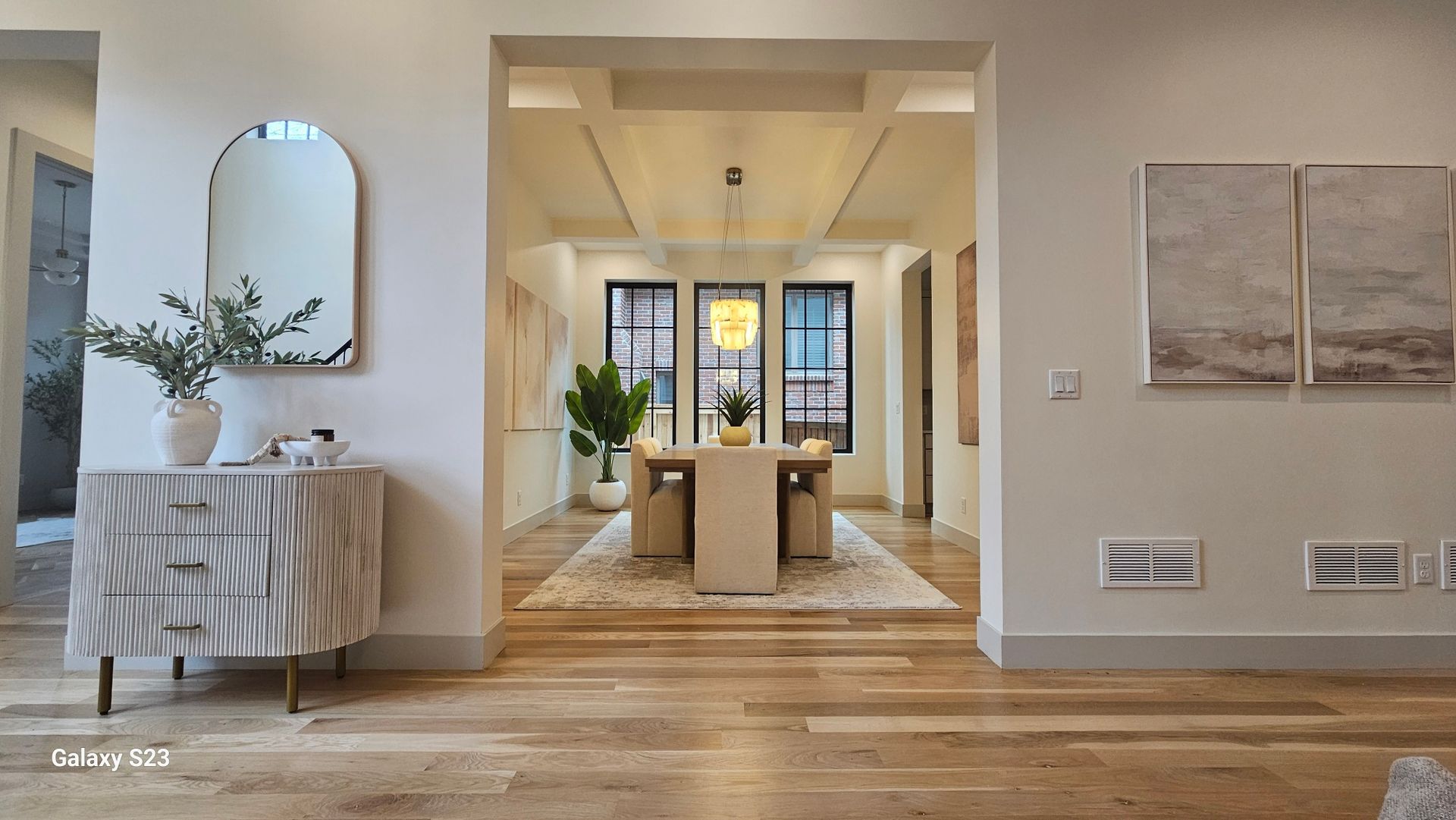 Entryway view: dining area visible through an archway. Features include a console table, mirror, and artwork.