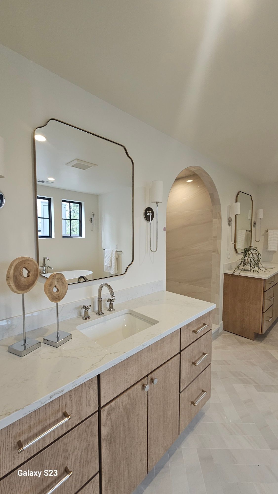 Modern bathroom with light wood cabinets, white countertops, and a large black-framed mirror.