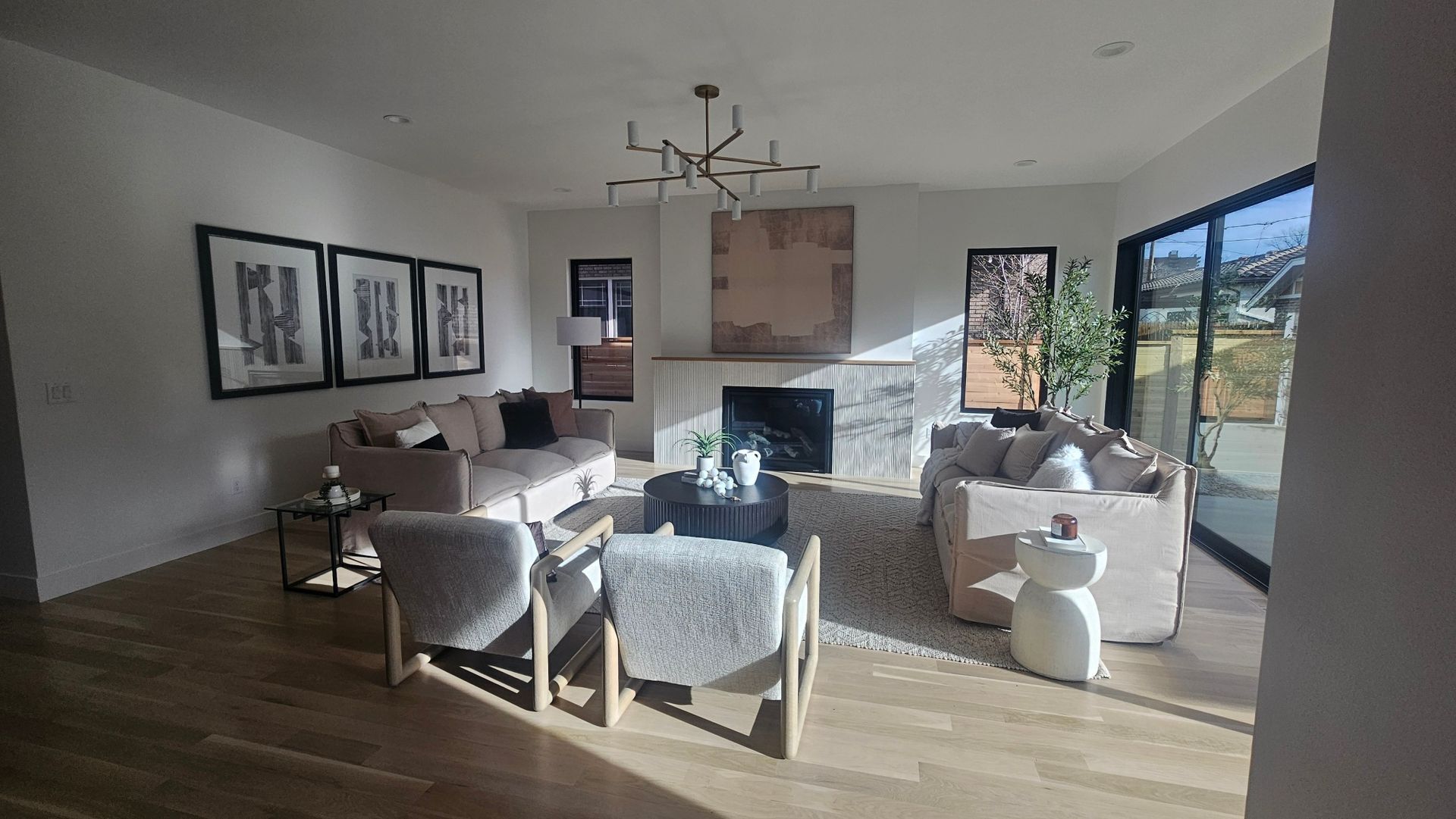 A bright, modern living room featuring two light-colored sofas, two accent chairs, a fireplace, and wall art.