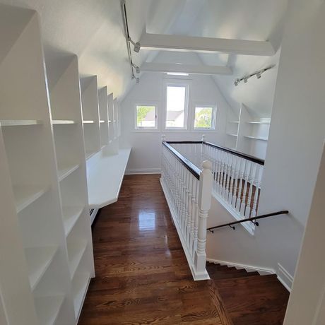 A hallway with hardwood floors and white shelves leading to a staircase.