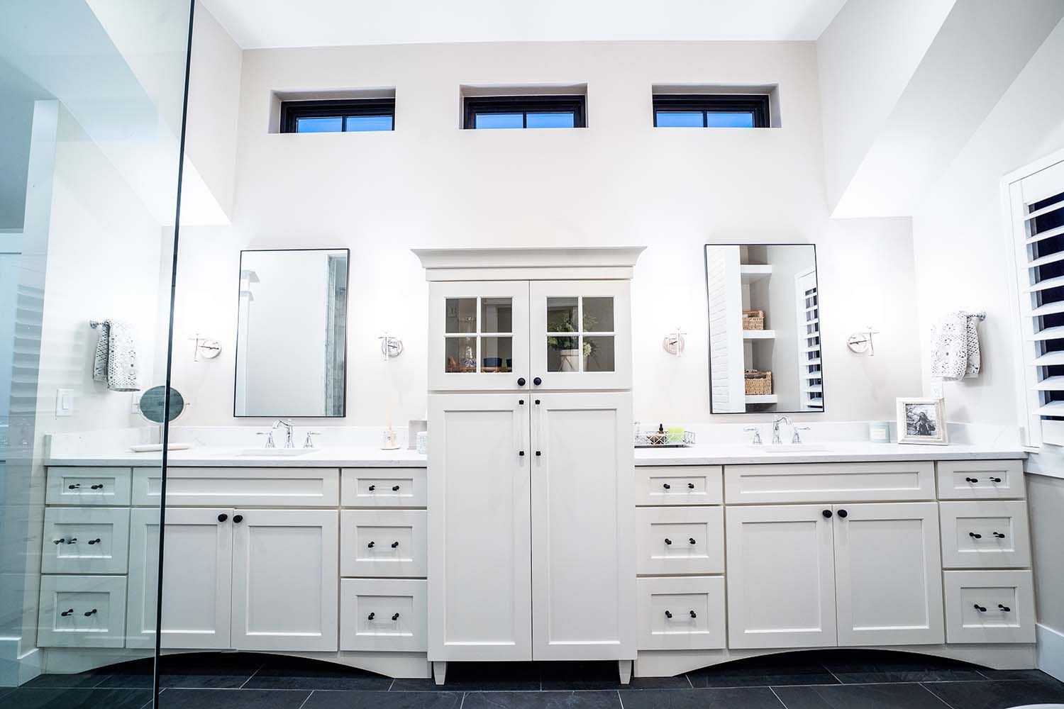 A bathroom with two sinks , two mirrors and a walk in shower.