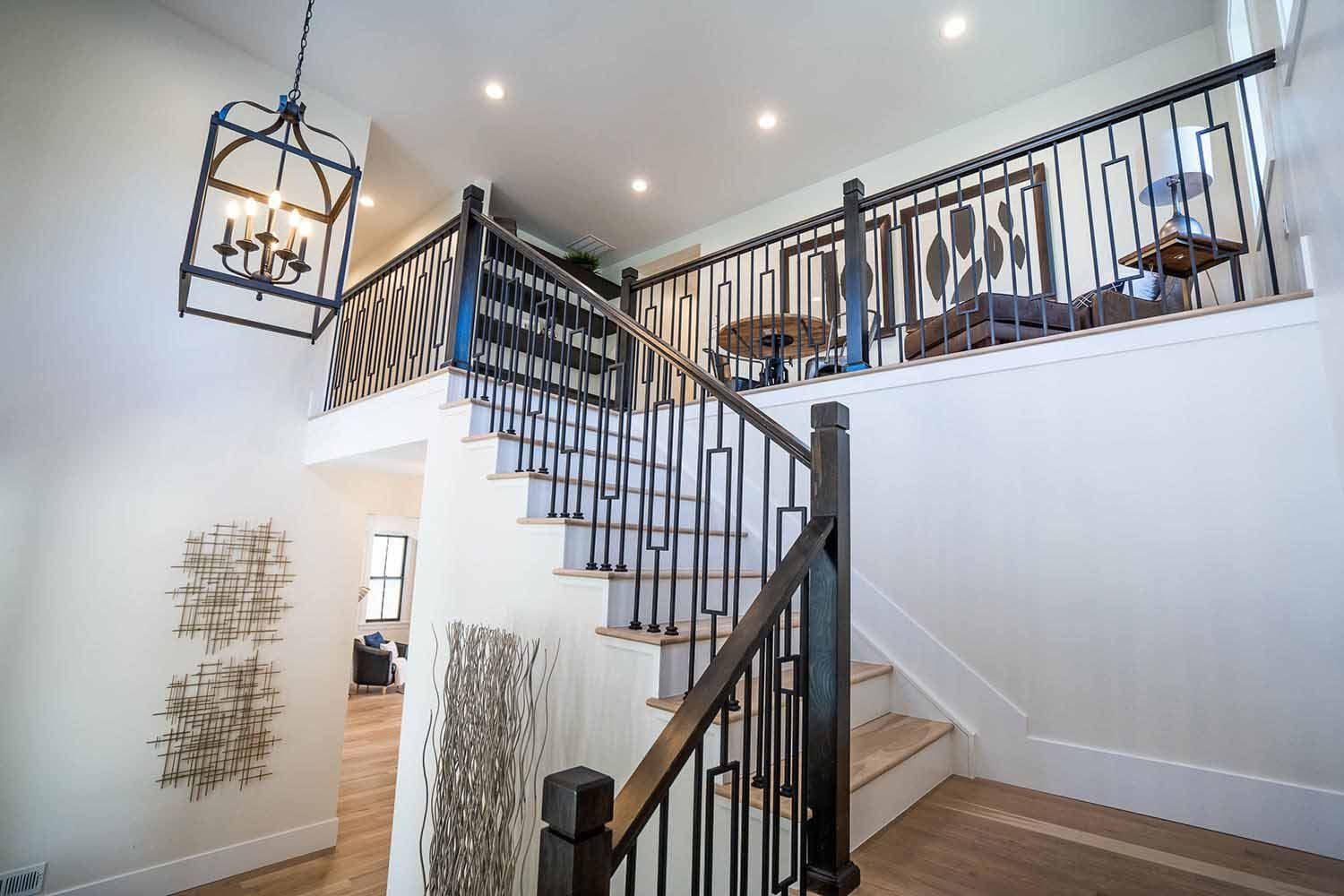 A staircase in a house with a black railing and a chandelier hanging from the ceiling.