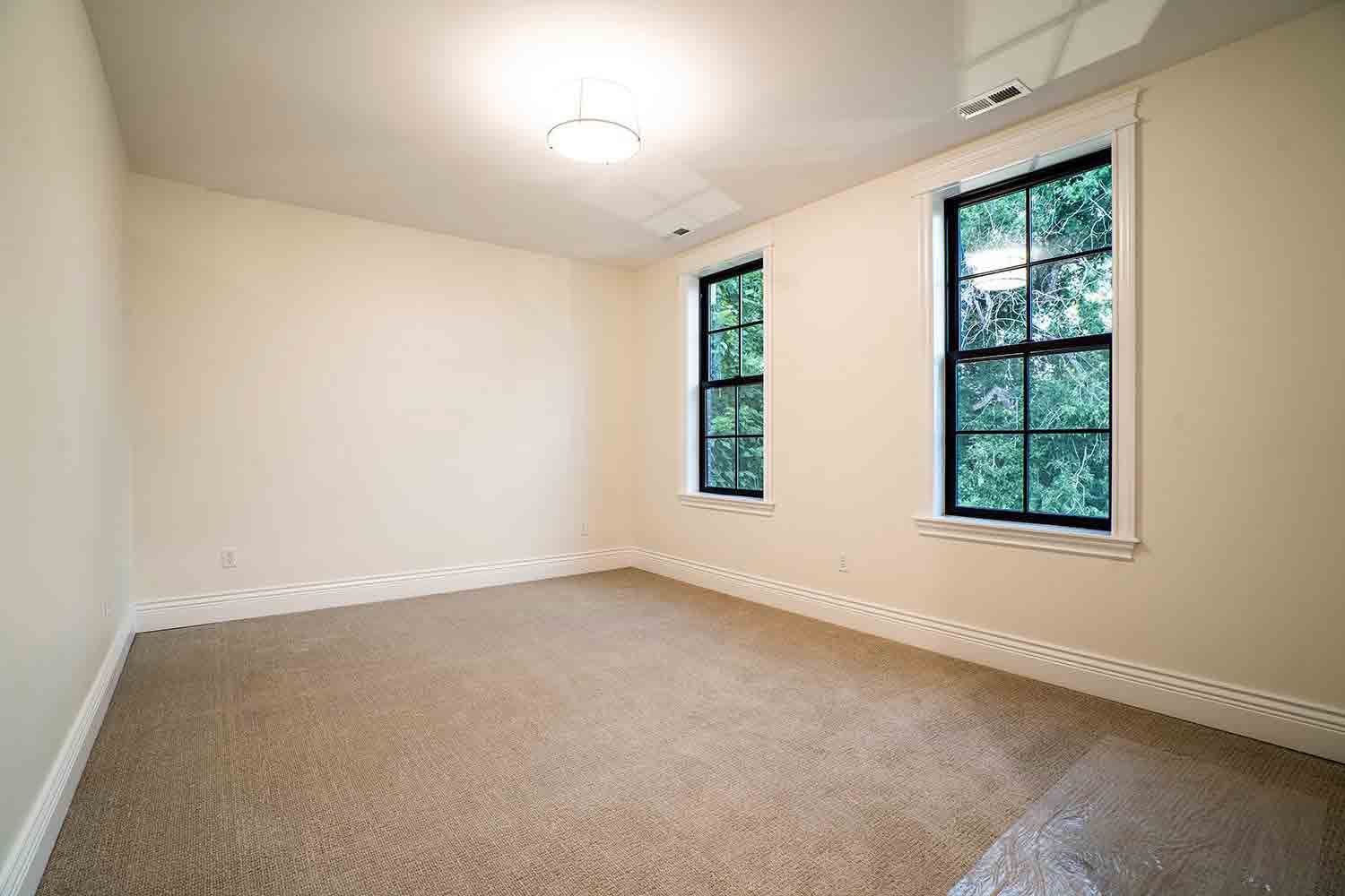 An empty room with two windows and a carpeted floor.