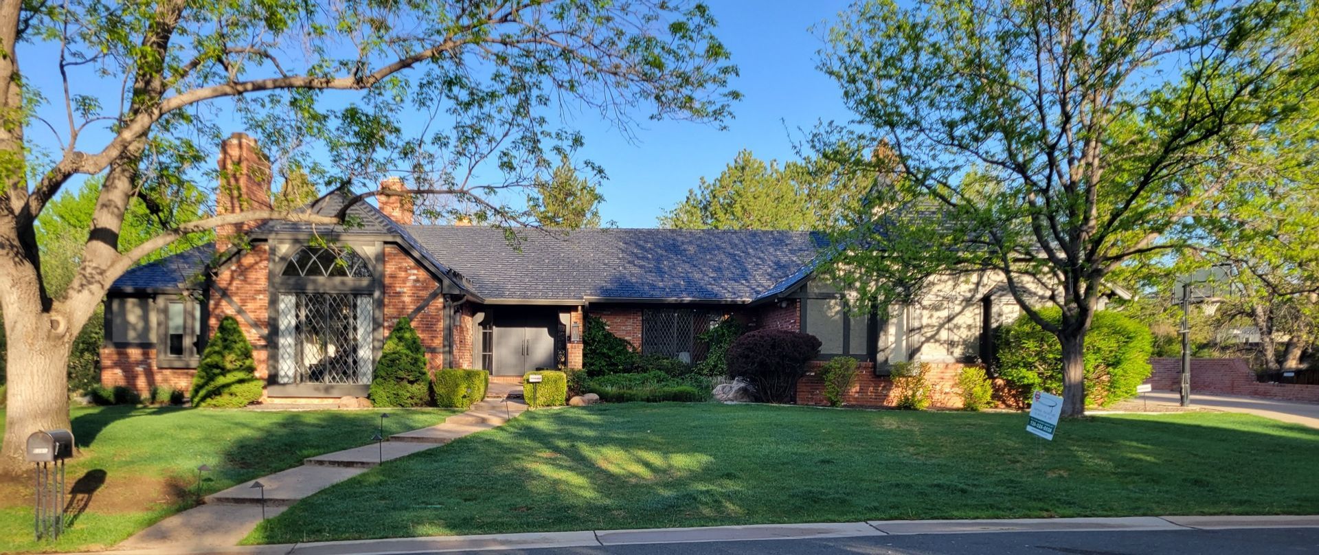 A large brick house with a black roof is surrounded by trees and grass.