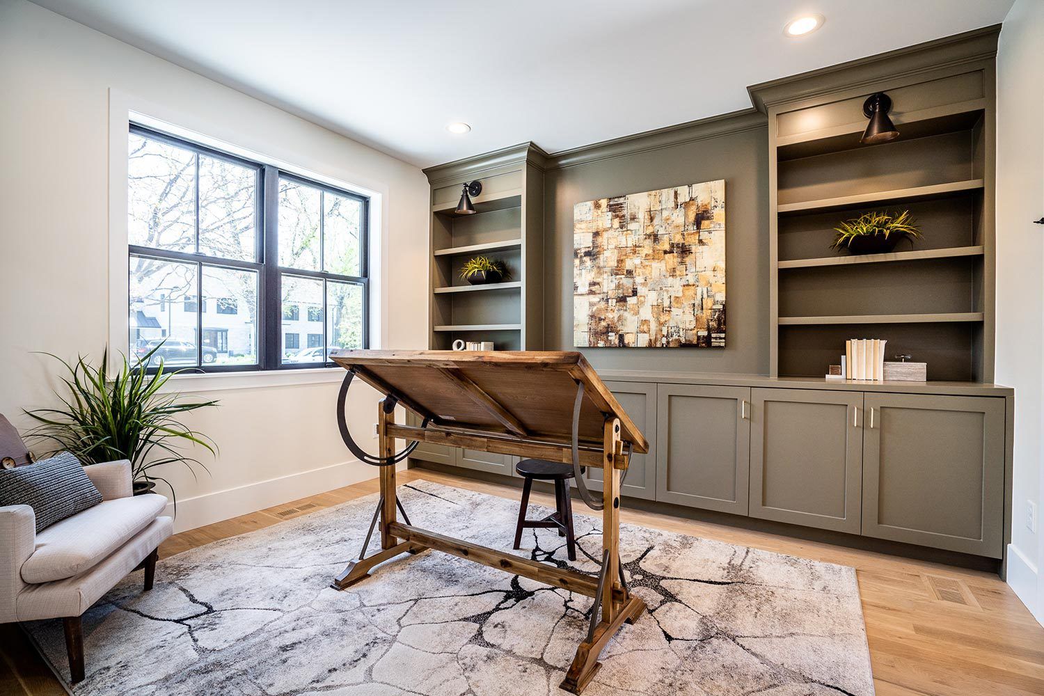 A living room with a desk , chair , rug and shelves.